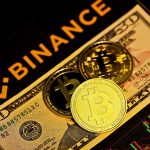 A photo of the Binance logo with a fifty dollar bill and a Bitcoin.