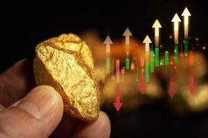 hand holding a gold nugget in front of a gold stock chart